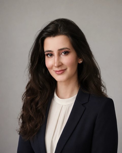 Talla Al-Dabak in dunklem Blazer und heller Bluse vor grauem Hintergrund